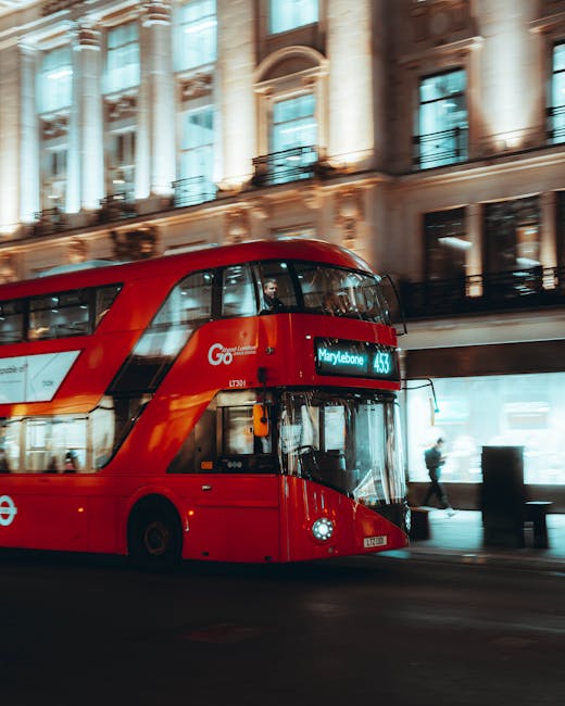 A red double-decker bus displaying the route number 453 and destination Marylebone is traveling along a city street illuminated by natural daylight. The bus features large front windows with reflections of surrounding buildings and people. In the background, there are historic multi-story buildings with ornate architectural details, tall windows, and balconies, indicating a typical London streetscape. The street is relatively quiet with a pedestrian walking on the pavement near the bus and other vehicles possibly out of view. The scene captures the typical urban environment where home relocation services by Movers Marylebone may involve coordinated furniture transport and moving logistics, with the bus potentially providing transportation for residents or serving as a reference point for nearby property access during a removal or house move in the W1 area.